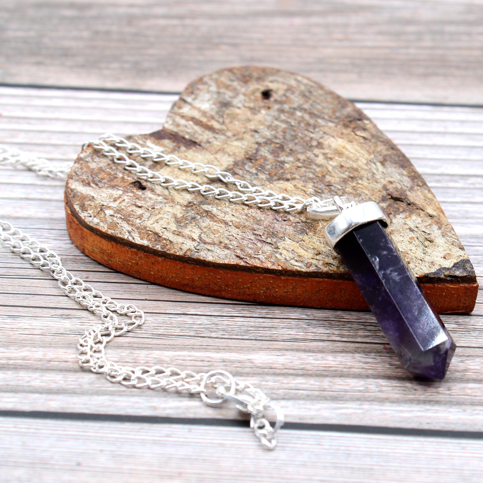 Colgante de piedras de amatista de tonos violetas sobre corazón de madera y cadena plateada en fondo de madera gris